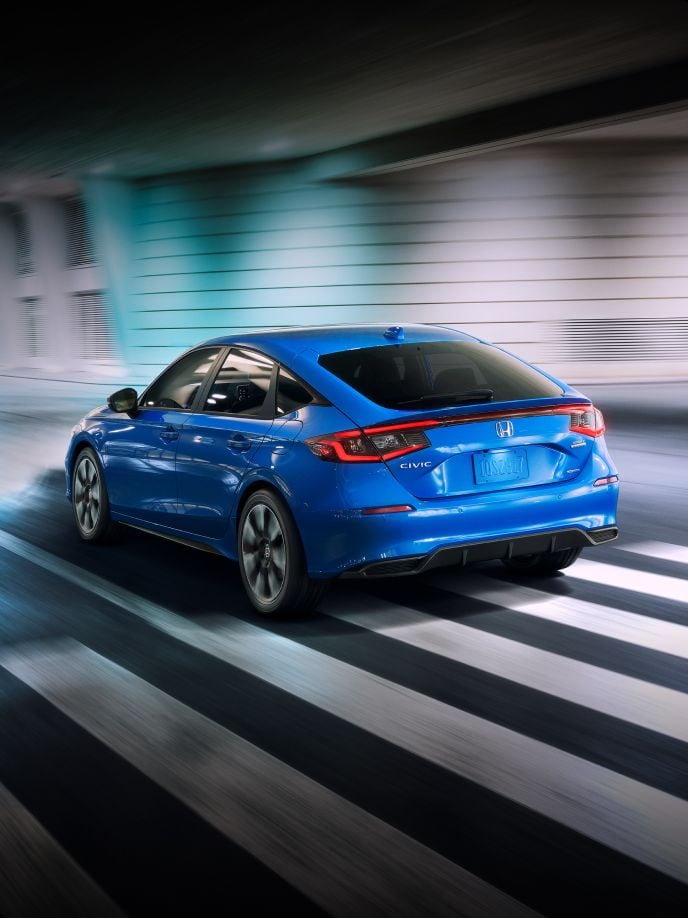 2025 Honda Civic Hatchback Sport Touring Hybrid in Boost Blue Pearl driving through underground tunnel