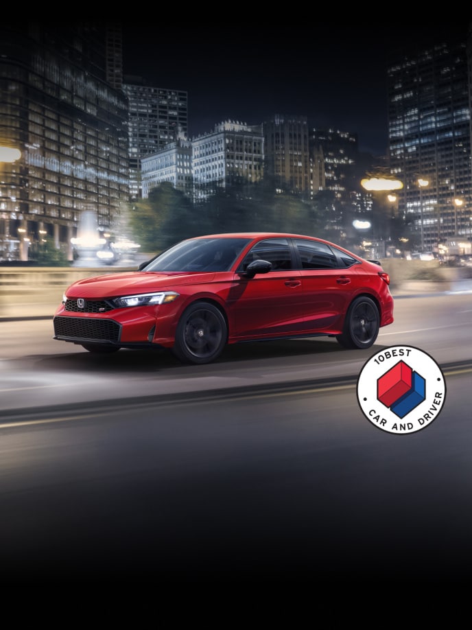 2026 Honda Civic Si Sedan in Rallye Red front 3/4 driving in a city at night with overlapping Car and Driver 10Best logo (Sporty Compact Sedan).
