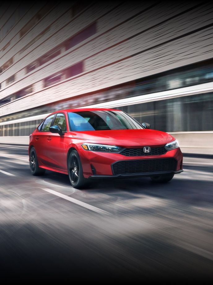 2026 Honda Civic Sedan Sport in Rallye Red with downtown landscape in the background