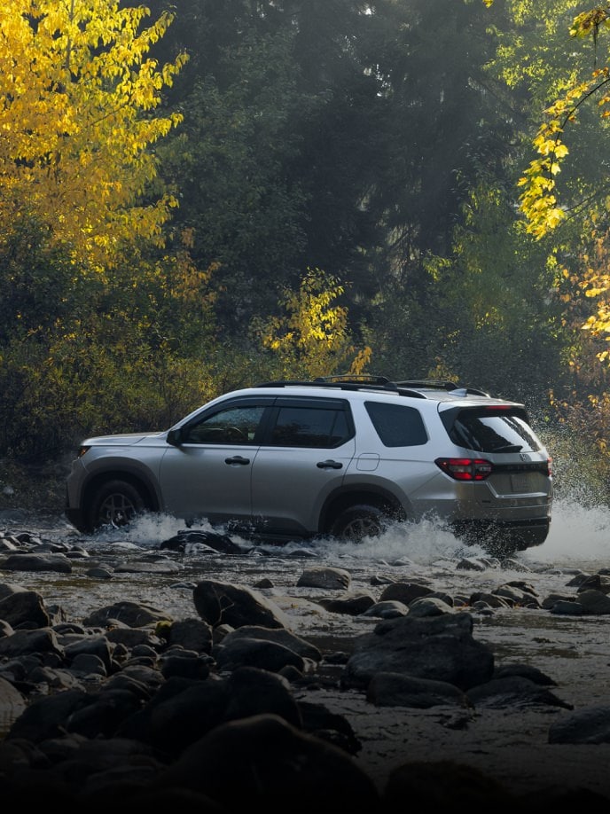 2025 Honda Pilot TrailSport in Lunar Silver Metallic, driving across a shallow river. 