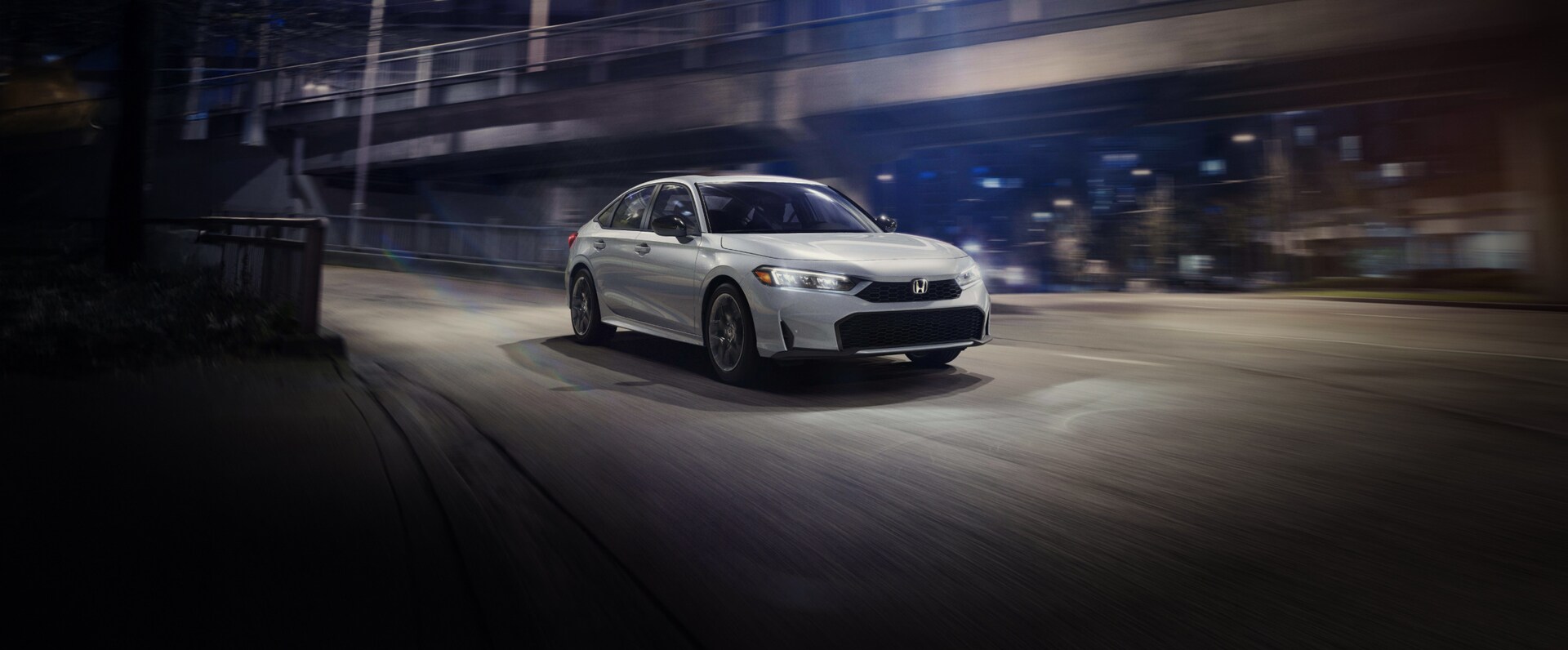 2026 Honda Civic Sedan Sport Touring Hybrid shown in Solar Silver Metallic in nighttime urban environment